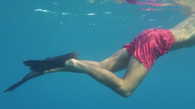 Ragazzo con maschera, pinne e costume rosso nuota nel mare sott'acqua