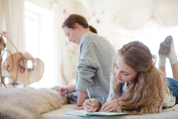 Obraz premium Two teenage girls on bed writing in notepads