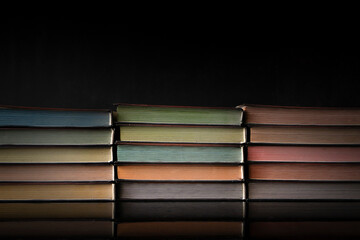 Old books with colored pages lie in stacks on a table on a very dark background