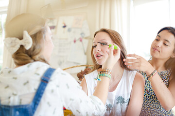 Three teenage girls doing make-up and brushing hair in bedroom