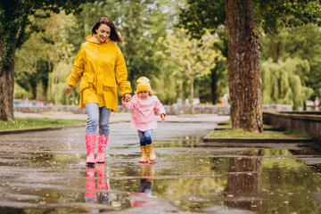 Mother with daughter having fun jumping in puddles