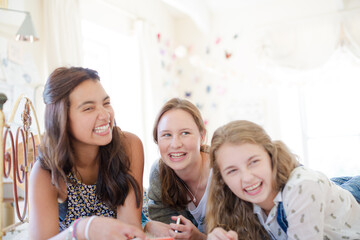 Three teenage girls using smart phone together while lying on bed in bedroom