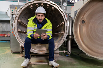 Naklejka na ściany i meble Male factory mechanic. Male engineer working with digital tablet for repairing, maintenance and checking steam boiler and automatic controls systems in the beverage factory. factory, industry concept
