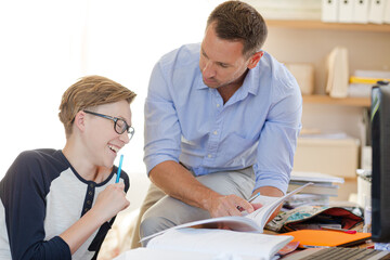 Father helping teenage son doing his homework in room