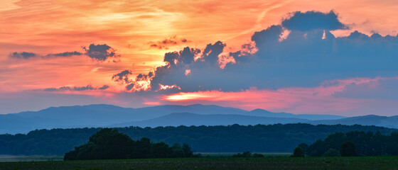 A colorful sunset over the mountains, the sun's rays illuminate the clouds on the horizon.