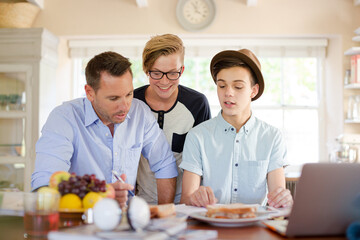 Teenage boys with father using laptop in dining room