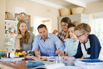 Teenagers with mid adult man sitting at table in dining room