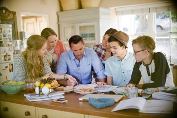 Teenagers with mid adult man sitting at table in dining room