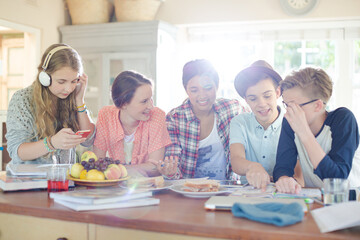 Group of smiling teenagers gathered around table in dining room