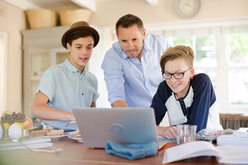 Fototapeta na wymiar Teenage boys with father using laptop in dining room