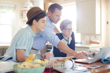 Teenage boys with father using laptop in dining room