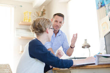 Father helping teenage son doing his homework in room