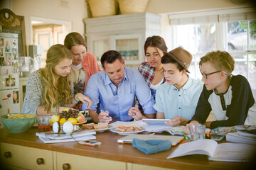 Teenagers with mid adult man sitting at table in dining room