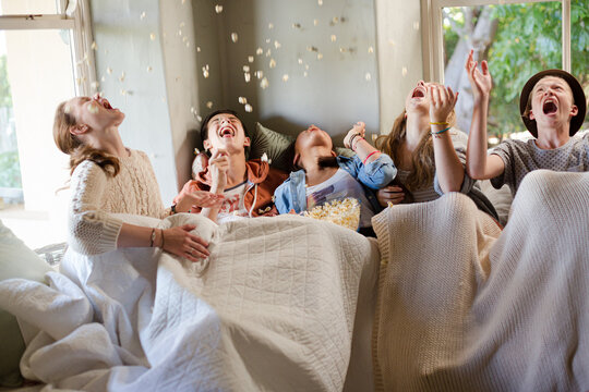 Group of teenagers throwing popcorn on themselves on sofa
