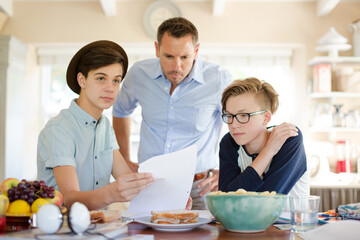 Teenage boys with father using laptop in dining room
