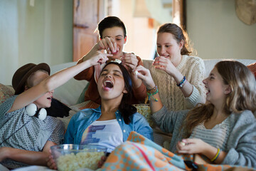 Group of teenagers throwing popcorn on themselves while sitting on sofa