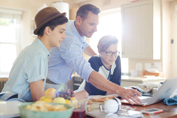Teenage boys with father using laptop in dining room