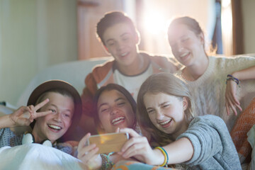 Group of teenagers taking selfie on sofa in living room