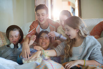 Group of teenagers throwing popcorn on themselves while sitting on sofa
