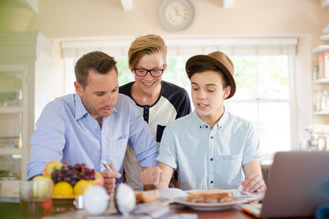 Teenage boys with father using laptop in dining room