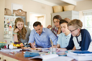 Teenagers with mid adult man sitting at table in dining room
