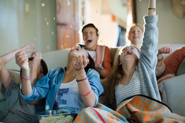 Group of teenagers throwing popcorn on themselves while sitting on sofa