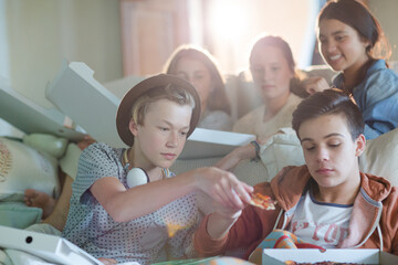 Group of teenagers eating pizza on sofa in living room