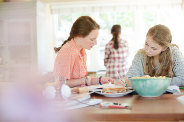 Teenage girls learning at table in kitchen