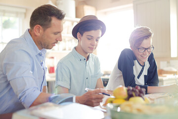 Teenage boys with father using laptop in dining room
