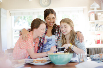 Three teenage girls looking at photograph while sitting at table
