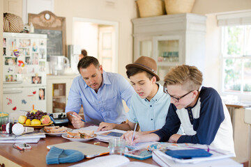Teenagers with mid adult man sitting at table in dining room