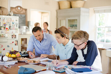 Teenagers with mid adult man sitting at table in dining room