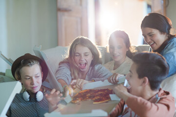 Group of teenagers opening pizza boxes on sofa in living room