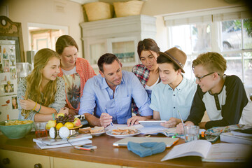 Teenagers with mid adult man sitting at table in dining room