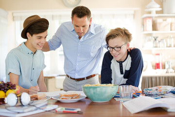 Teenage boys with father using laptop in dining room