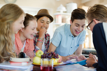 Group of teenagers using together digital tablet at table in kitchen