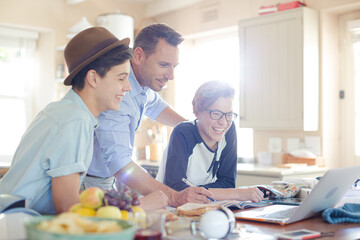 Teenage boys with father using laptop in dining room