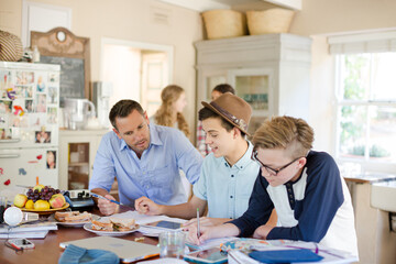 Teenagers with mid adult man sitting at table in dining room