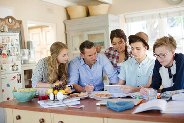 Teenagers with mid adult man sitting at table in dining room