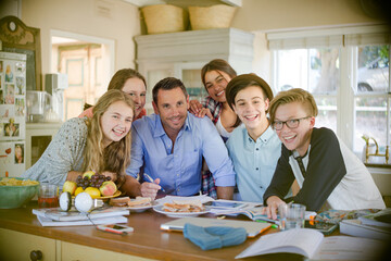 Group of teenagers with mid adult man sitting at table in dining room