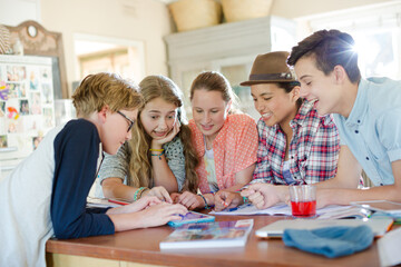 Fototapeta premium Group of teenagers using together digital tablet at table in kitchen