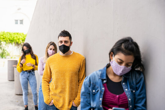 Group of friends keeping social distance while waiting for going in shop in lined during global pandemic from Coronavirus Covid-19 wearing face masks near a gray wall - Copy space - Colorful dresses