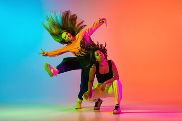 Two beautiful hip-hop girls dancing on gradient blue orange backlground in neon - obrazy, fototapety, plakaty