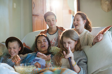 Group of teenagers having fun while watching tv on sofa