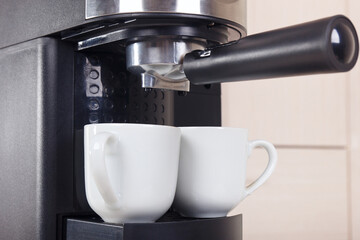 Two white cups for coffee under horn coffee maker.
