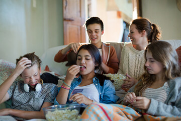 Group of teenagers throwing popcorn on themselves while sitting on sofa