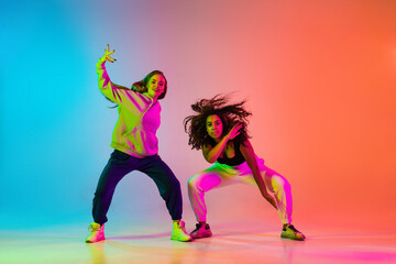 Two beautiful stylish hip-hop dancers on colorful gradient background in neon lights