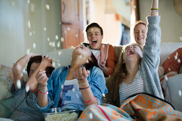 Group of teenagers throwing popcorn on themselves while sitting on sofa