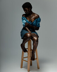 Studio shot of young woman in blue silk top and mini skirt sitting on stool