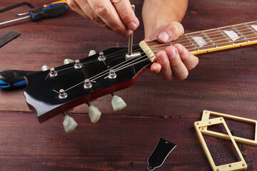 Guitar repairman adjusts the trussrod on electric guitar at workplace.